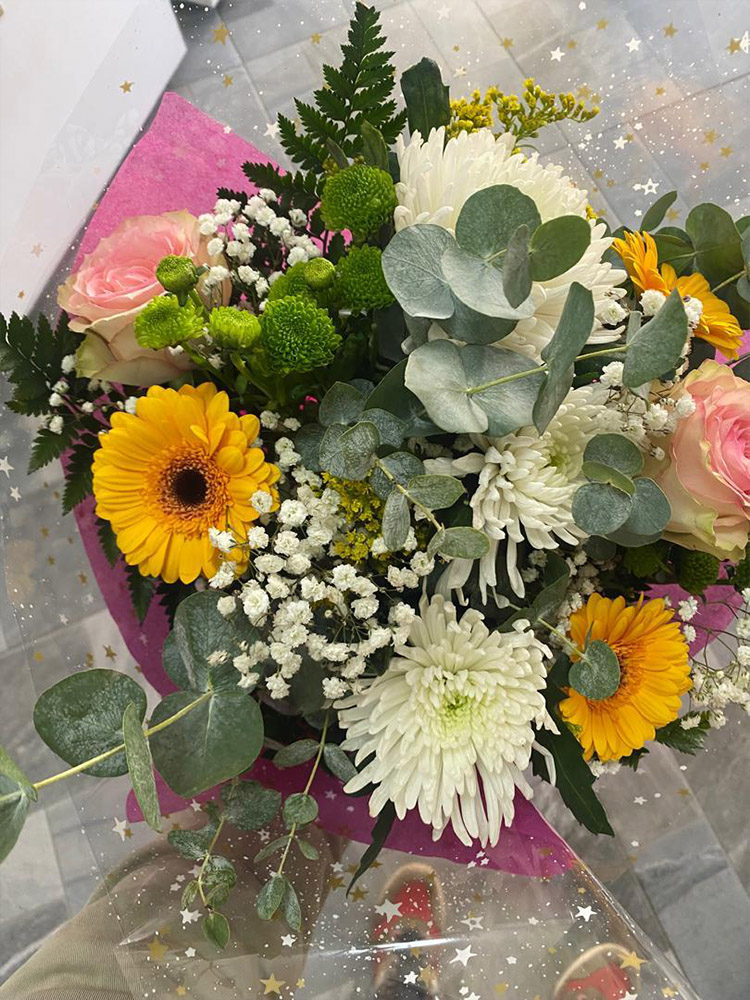 Bouquet "Eclat de bonheur" avec gerberas jaunes, chrysanthèmes blancs et roses pâles dans un emballage étoilé.