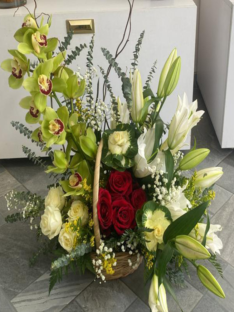 Magie d'Affection, Panier floral avec orchidées vertes, roses rouges, lys blancs et eucalyptus dans une élégante corbeille d'osier.